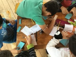 Draufsicht auf einen Tisch, an dem Kinder mit Papiermaterialien malen und basteln