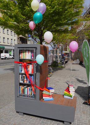 Bild von der Eröffnung des Verschenkschranks: eine stabile Box voller Bücherregale, mit Luftballons geschmückt