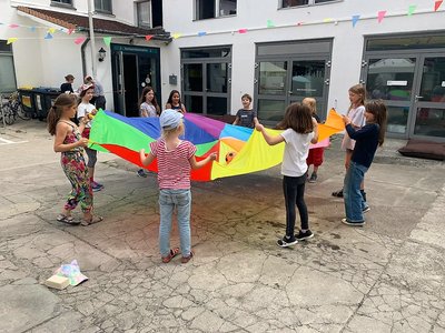 Bild von der Bauwoche: Kinder halten draußen im Hof zusammen ein buntes Tuch.
